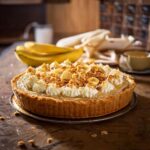 Fully prepared no-bake peanut butter banana cream pie garnished with whipped cream, bananas, and crushed peanuts on a marble countertop